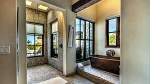 A bathroom with stone walls, a large window, a bathtub, and a towel rack.