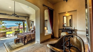 A spacious bedroom with a large bed, a bathtub, and a view of the ocean.