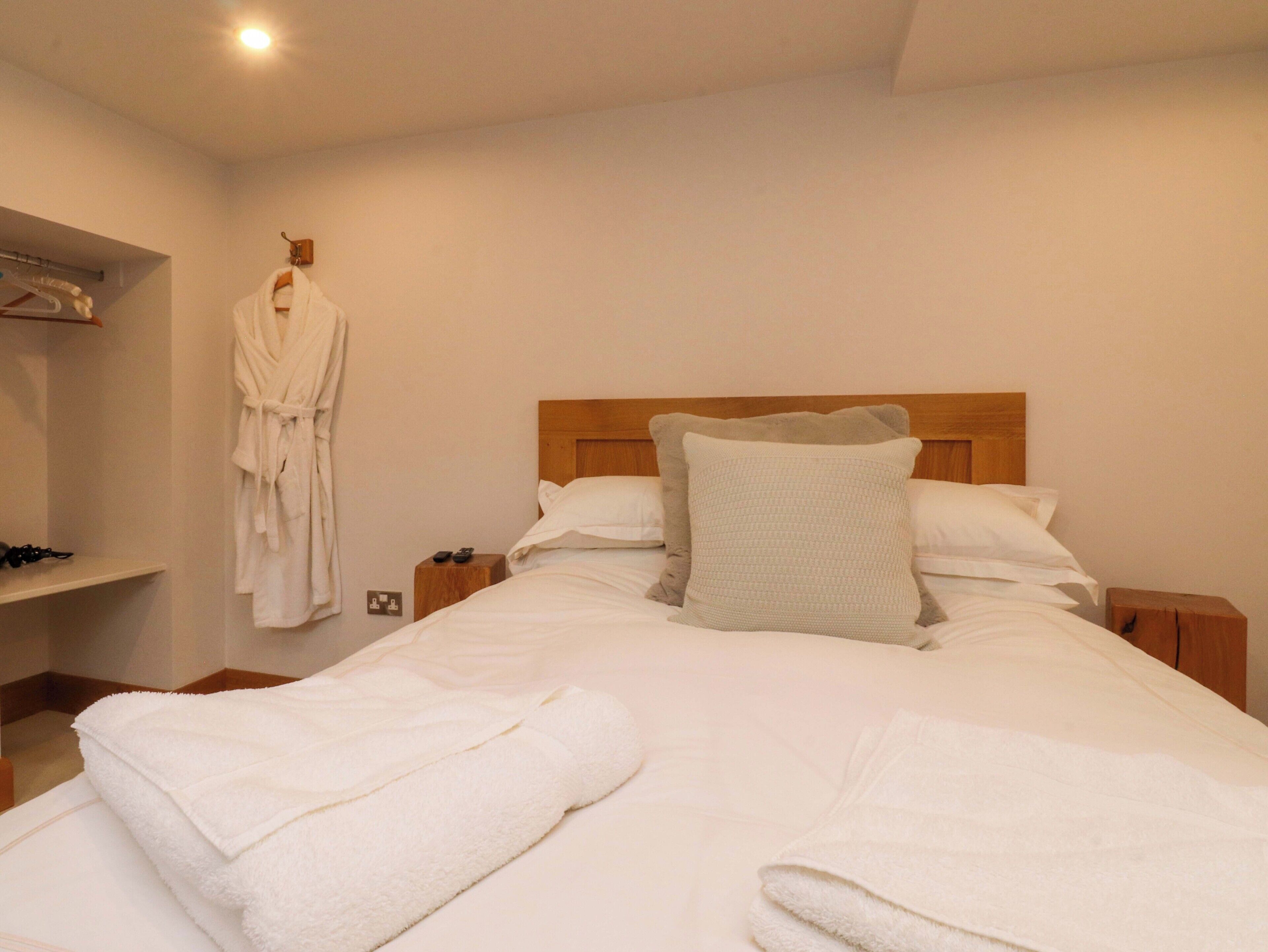 A neatly made bed with white linens and towels, a wooden headboard, and a robe hanging on a hook.