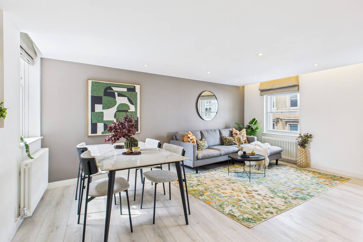 Un salon moderne avec une table à manger, un canapé gris et un tapis coloré.