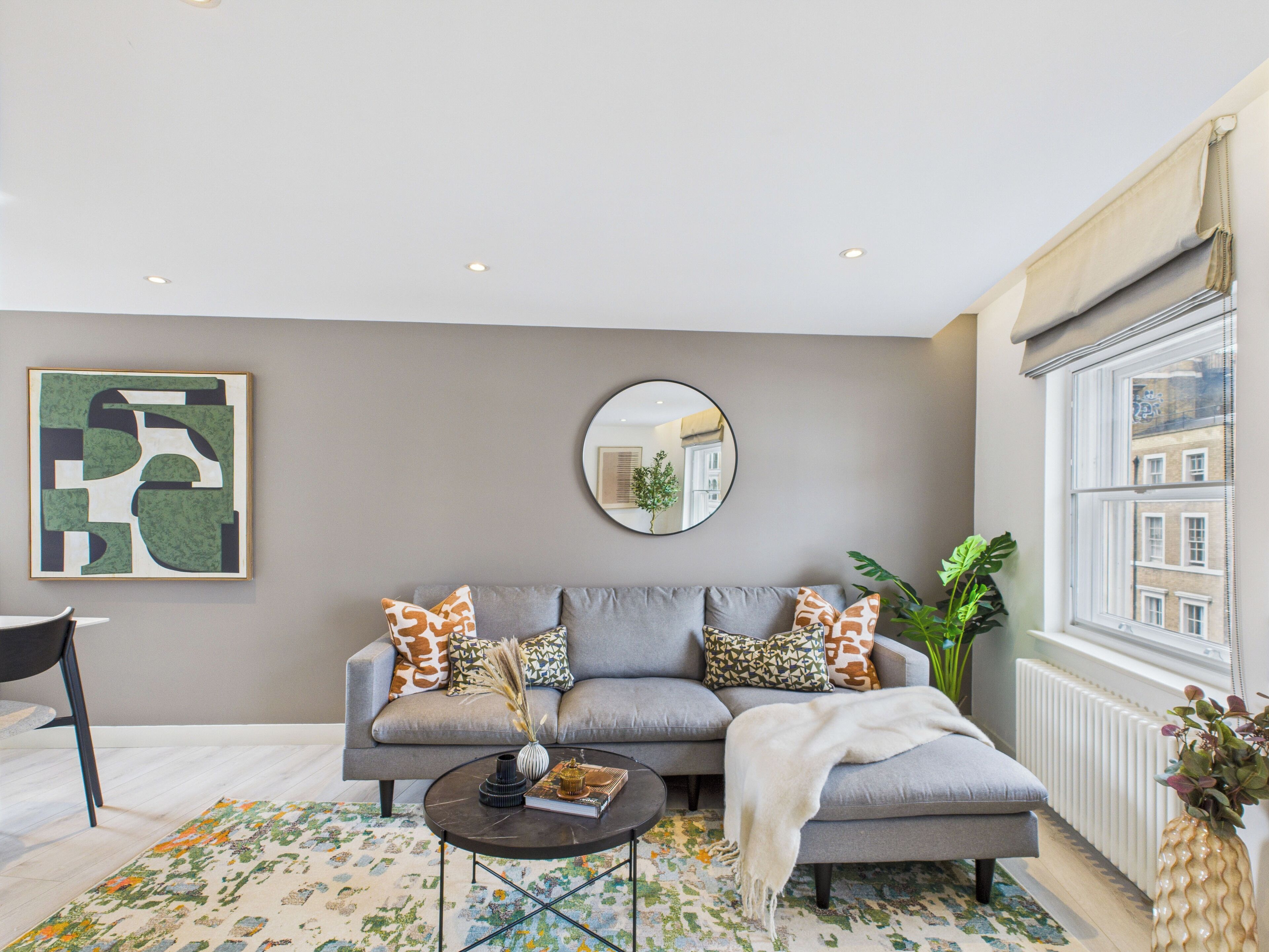 A modern living room with a grey sofa, a round mirror, and a coffee table with books and a vase.