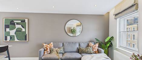 A modern living room with a grey sofa, a round mirror, and a coffee table with books and a vase.