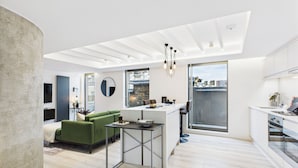 Un apartamento moderno con cocina, comedor y sala de estar. Cuenta con un ventanal grande, un sofá verde y una pequeña mesa.