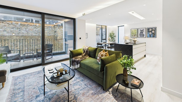 Una sala de estar moderna con un sofá verde, una mesa de centro de vidrio y un comedor al fondo.