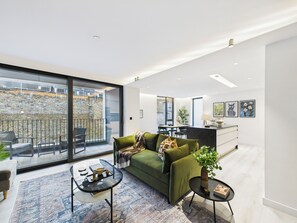 A modern living room with a green sofa, a glass coffee table, and a dining area in the background. - Be London - Borough Market Residences (London)