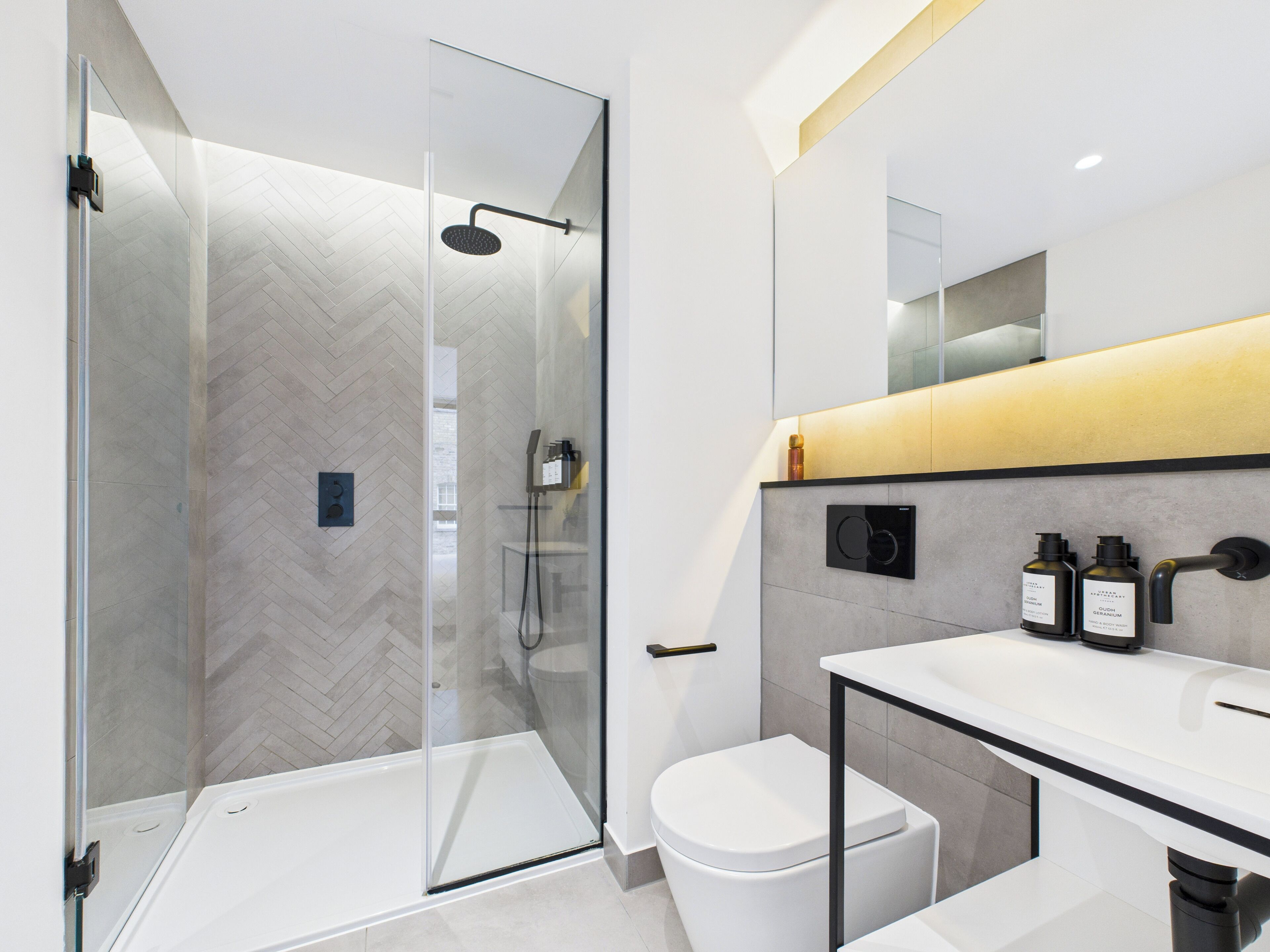 Een moderne badkamer met een douchecabine van glas, een wit toilet en een wastafel met een spiegel en twee flessen shampoo.
