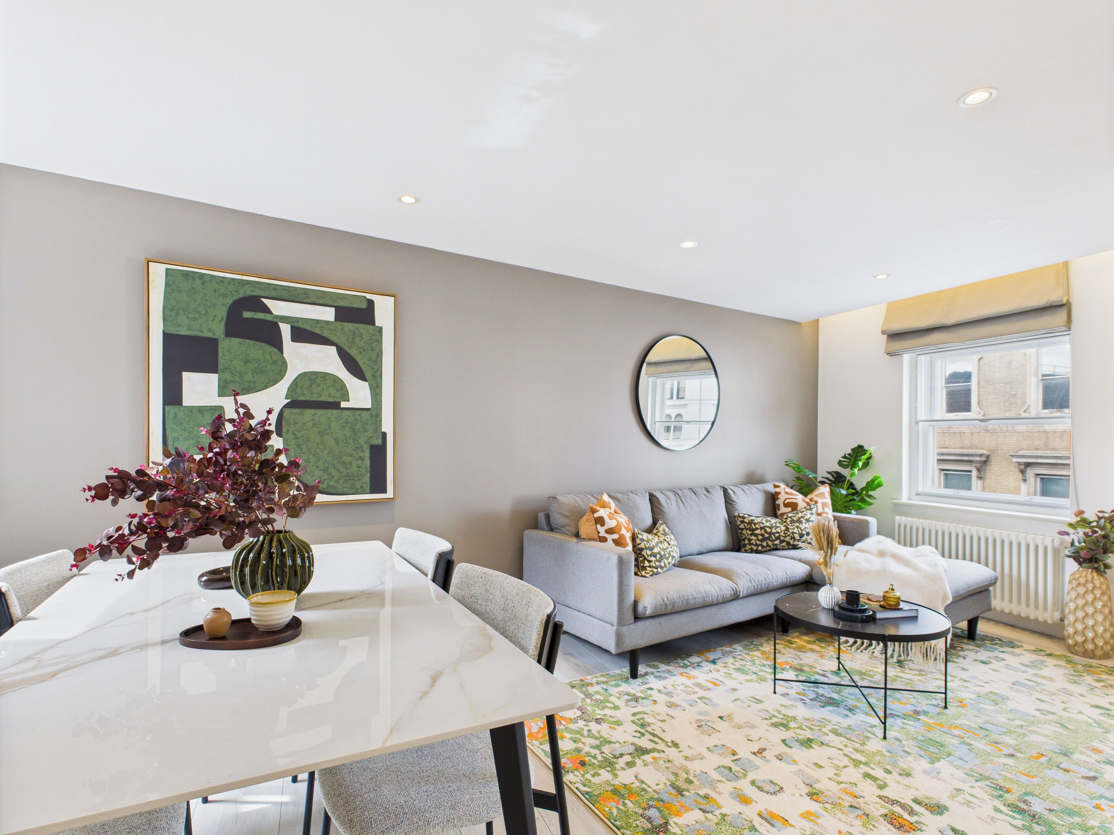 A modern living room with a grey sofa, a dining table, and a colorful rug.