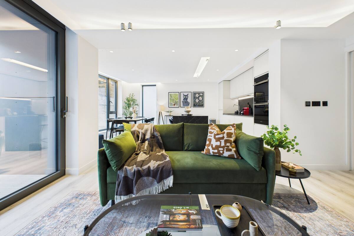 Un salon moderne avec un canapé vert, une table basse et, au fond, une vue sur la cuisine.