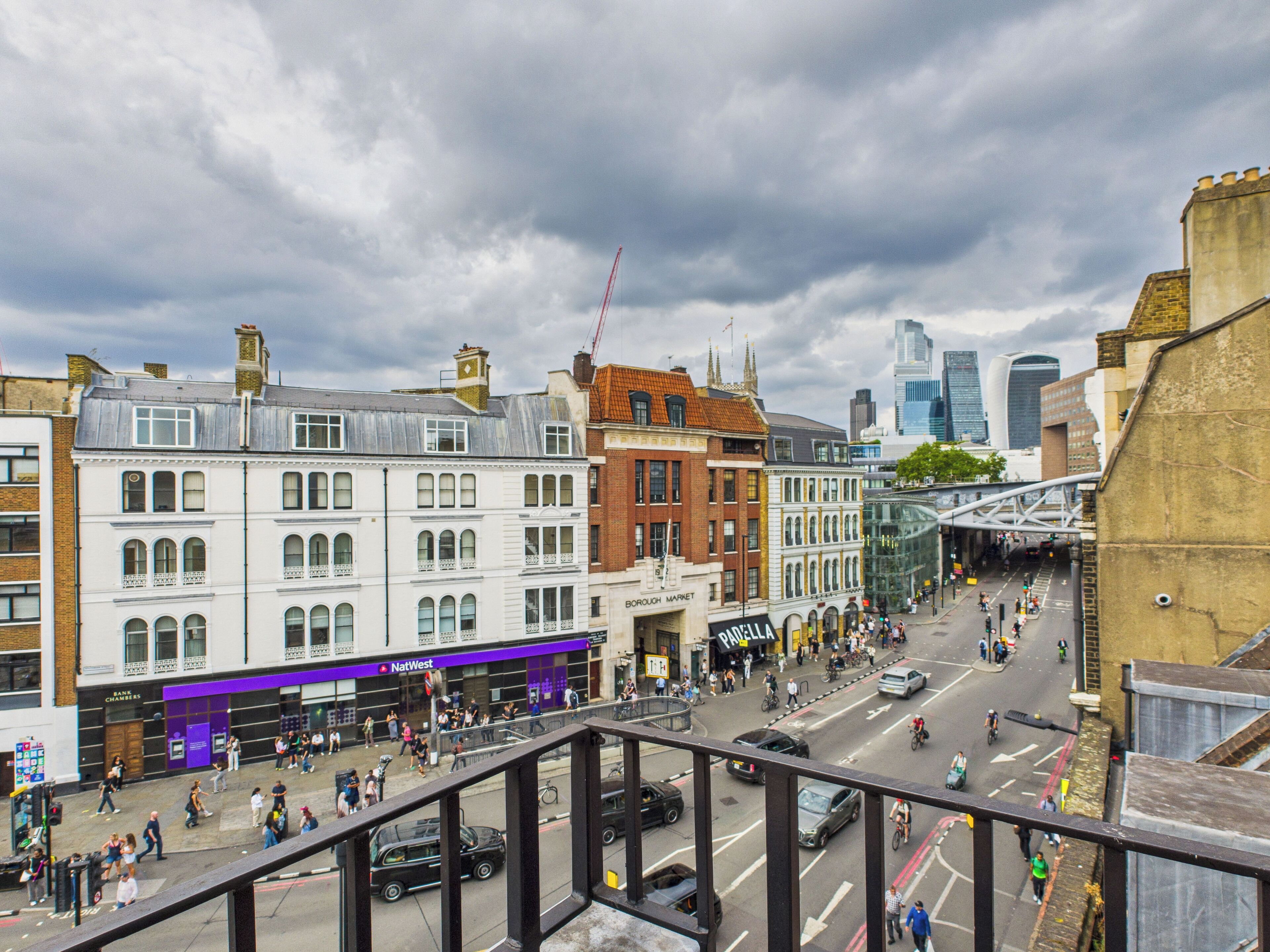 A busy urban street with historic buildings, a modern glass structure, and a pedestrian walkway.