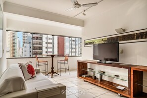 A modern living room with a sofa, a TV, a wooden entertainment unit, and a dining table with chairs. - Beachfront apt BC Center Close to Attract. Aco803 (Balneário Camboriú)