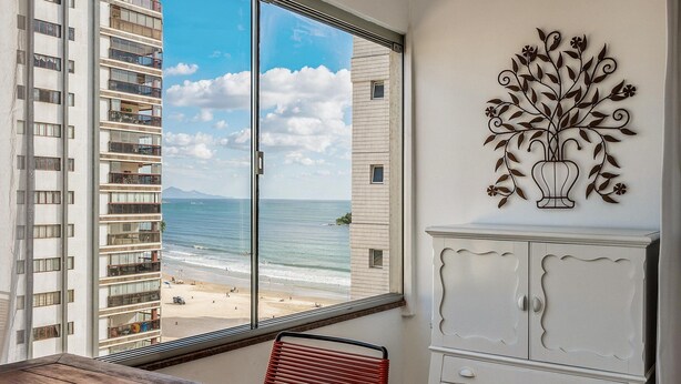 A room with a large window overlooking a beach, a white cabinet, and a decorative metal piece on the wall. - Beachfront apt BC Center Close to Attract. Aco803 (Balneário Camboriú)