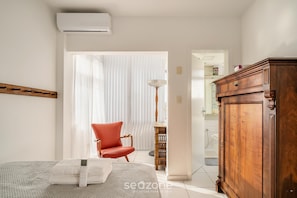 A bedroom with a bed, a red chair, a wooden wardrobe, and a bedside table with a lamp. - Beachfront apt BC Center Close to Attract. Aco803 (Balneário Camboriú)
