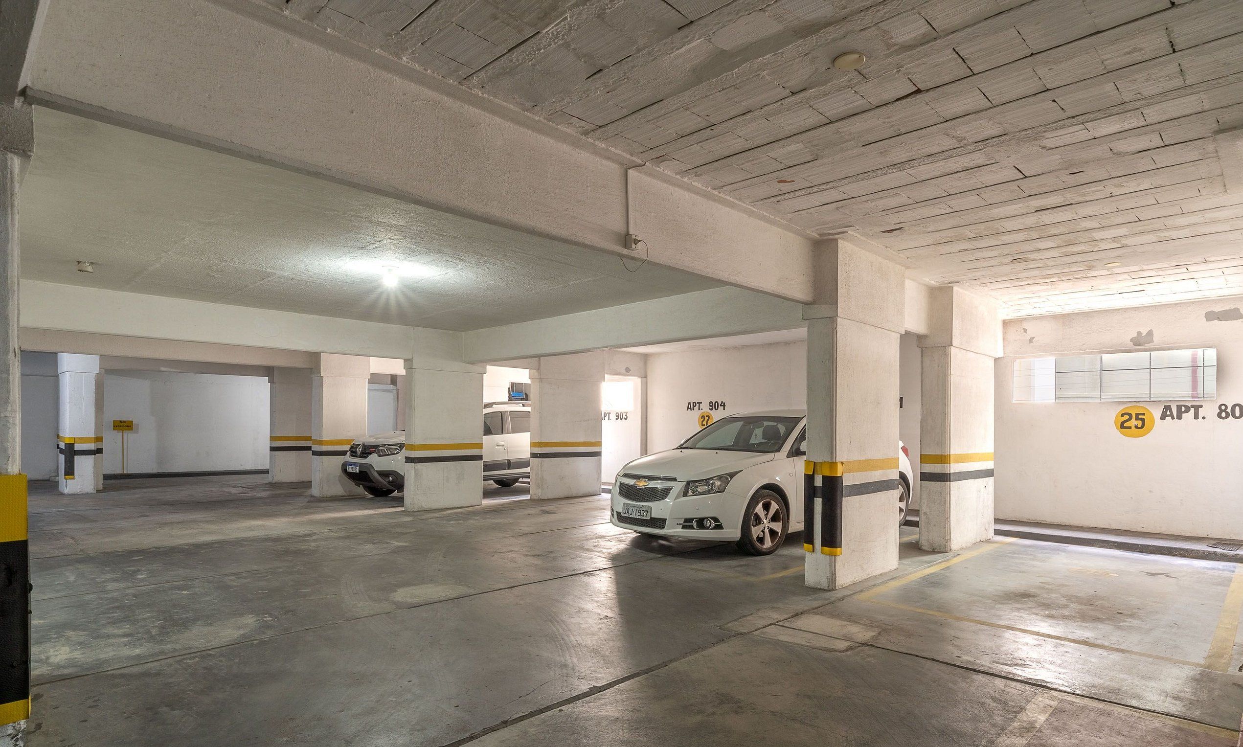 Eine mehrgeschossige Parkgarage mit Betonpfeilern, ausgewiesenen Stellplätzen und einem weißen Auto auf einem Platz.