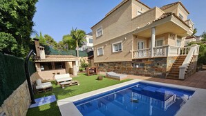 A two-story house with a swimming pool, a patio with outdoor furniture, and a stone staircase.