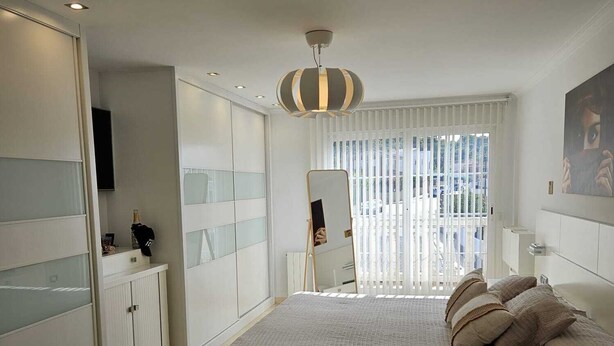 A modern bedroom with a large bed, a wardrobe, a vanity, and a window with blinds.