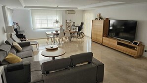 A modern living room with a sofa, a coffee table, a TV, and a dining area with chairs and a table.