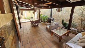 An outdoor patio with a stone wall, wooden furniture, and a ceiling fan.