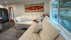 Una sala moderna con un sofá seccional color beige, una mesita auxiliar y un ventanal con vistas a un jardín.
