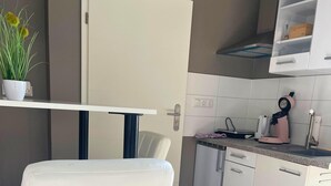 Uma cozinha moderna com armários brancos, uma cadeira branca, uma mesa branca e uma cafeteira rosa.