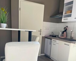 A modern kitchen with white cabinets, a white chair, a white table, and a pink coffee machine.