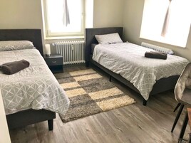 A small, modern bedroom with two beds, a wooden floor, and a checkered rug.