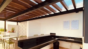 Une cuisine moderne avec un plan de travail noir, des poutres en bois au plafond et un revêtement mural blanc.