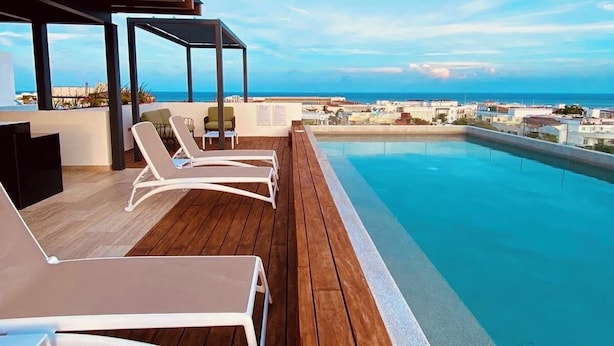 Un espace piscine aménagé sur le toit, avec des chaises longues et une terrasse en bois offrant une vue panoramique sur la ville et la mer.