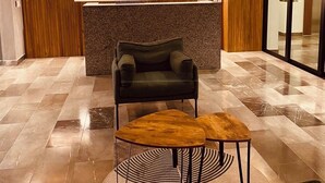 Un espace d’accueil avec un mur en bois, un panneau néon indiquant « Duna », un comptoir d’accueil, un canapé vert et une petite table en bois.