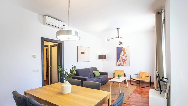 Ein modernes Wohnzimmer mit einer Couch, einem Esstisch mit Stühlen, einer Stehlampe und einem Bild an der Wand.