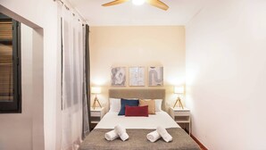 Ein Hotelzimmer mit einem Bett, zwei Nachttischen mit Lampen, einem Deckenventilator und Bildern an der Wand.