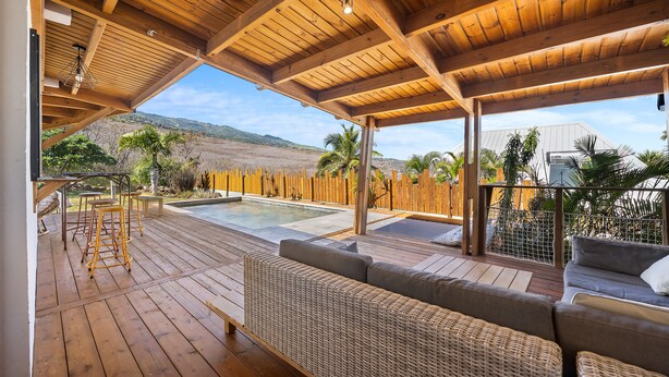 Una terraza de madera con piscina, mobiliario exterior y vistas al paisaje.