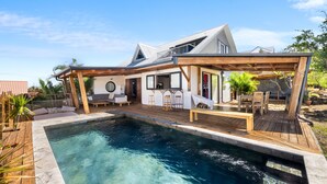 Una casa moderna con piscina, terraza de madera y zona de estar al aire libre.