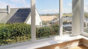 Una habitación con un ventanal grande que da a una playa, paneles solares en el techo y vistas de un pueblo costero.