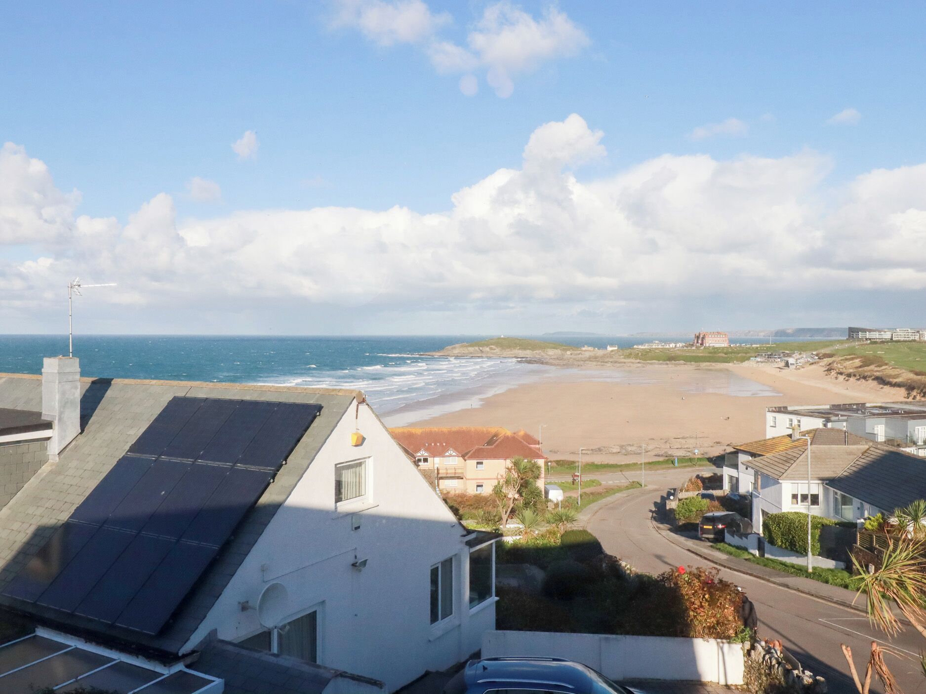 A coastal residential area with a beach, houses with solar panels, and a clear sky.
