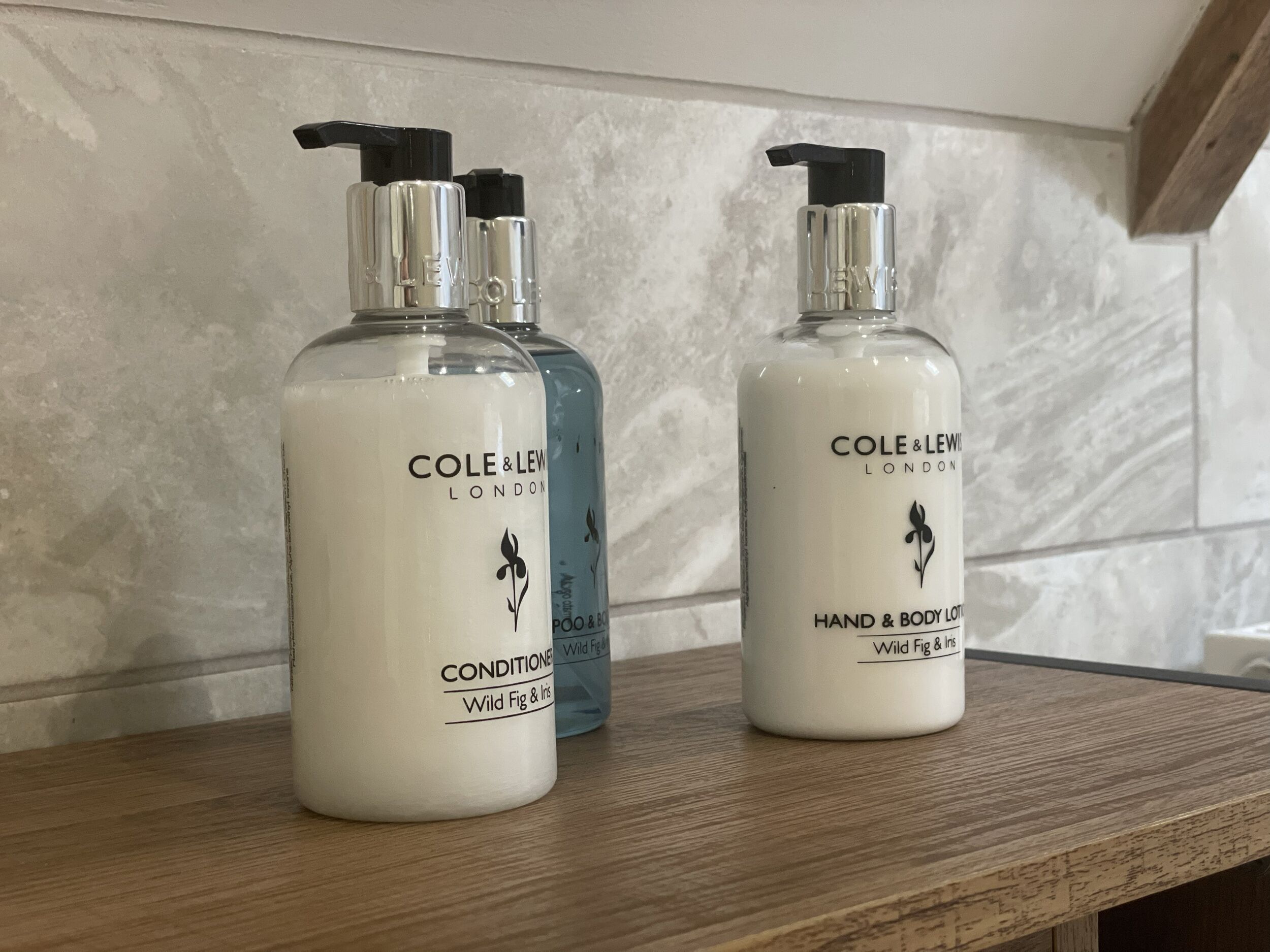 Tres botellas de loción corporal y de manos Cole & Lew London sobre una superficie de madera.