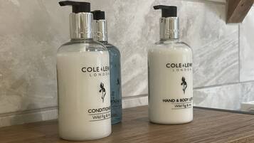 Tres botellas de loción corporal y de manos Cole & Lew London sobre una superficie de madera.