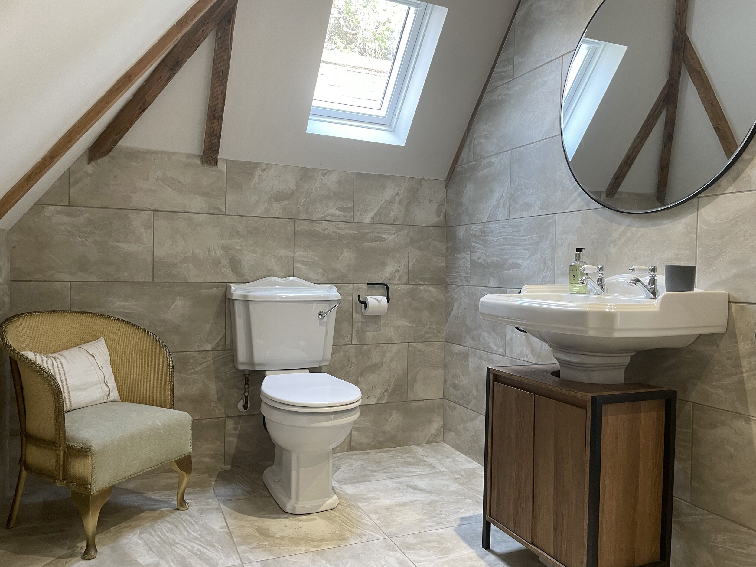A bathroom with a toilet, sink, and chair.