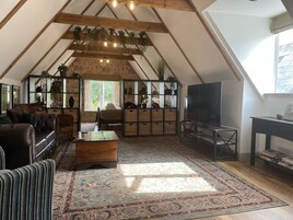 Un loft amplio con techo alto, vigas de madera a la vista, un ventanal grande y una zona de estar acogedora con televisor y estanterías.
