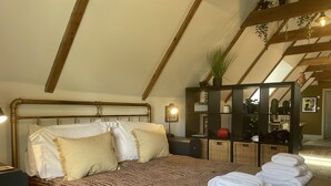 Un dormitorio con una cama grande, una mesita de noche, un espejo y una estantería con plantas y adornos.