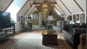 Un loft amplio con techos altos, vigas de madera a la vista, un televisor grande, un comedor y una zona de estar acogedora con un tapiz estampado.