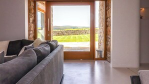 A modern living room with a grey sofa, a stone wall, and a large glass door leading to a lawn. - Carden Laithe Barn (Skipton)