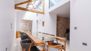A modern dining area with a long wooden table and chairs, a glass-top table, and a stone wall in the background. - Carden Laithe Barn (Skipton)