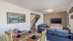 A dining area with a table set for four, a sofa, a TV, and a staircase leading to another room. - House in Cabo Frio 200m From the Beach Adp001 (Cabo Frio)