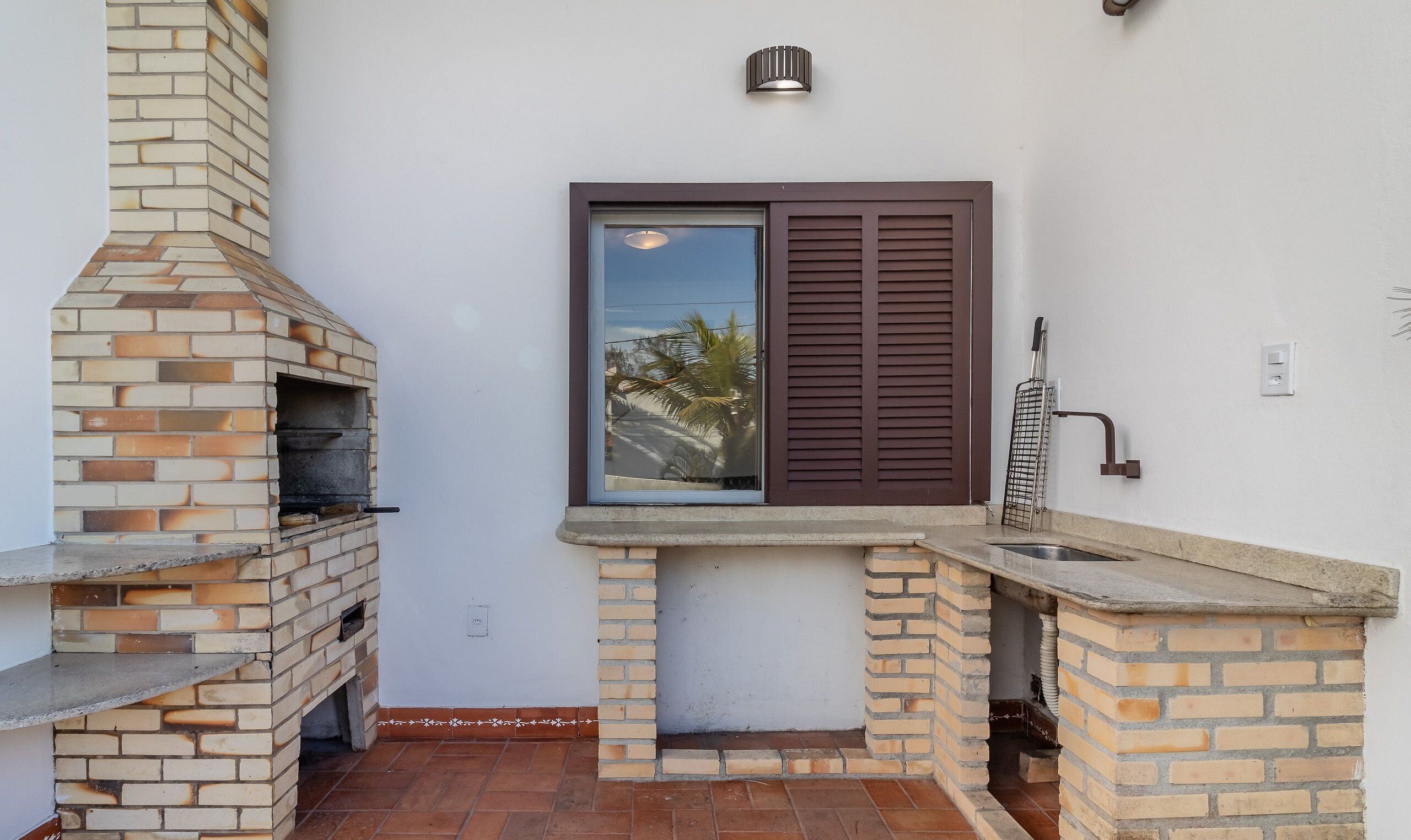 A brick-built outdoor kitchen with a chimney, a window with shutters, and a sink.