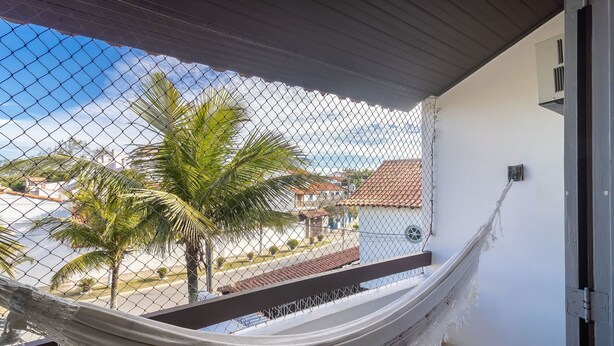 A hammock on a balcony with a view of palm trees and buildings. - House in Cabo Frio 200m From the Beach Adp001 (Cabo Frio)