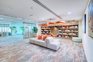 A modern lobby with a sectional sofa, a large bookshelf, and a hanging spherical light fixture.