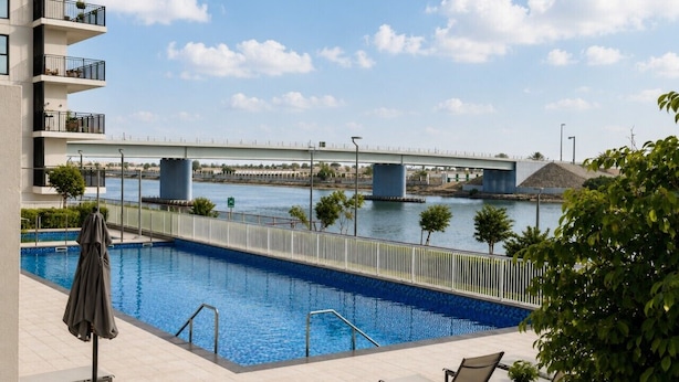 Una piscina con vista su un ponte, sedie a sdraio e un edificio con balconi.