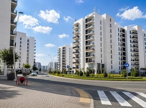 A modern urban street with high-rise residential buildings, a pedestrian crossing, and directional signs.