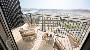 A balcony with a view of a cityscape, two wicker chairs, a small table with food and drinks, and a railing. - 1BDR F1 Yas Island | Stunning Views on the Circuit (Abu Dhabi)