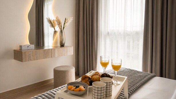 A hotel room with a bed, a bedside table with a tray of breakfast, a mirror, and a window with curtains. - 1BDR F1 Yas Island | Stunning Views on the Circuit (Abu Dhabi)